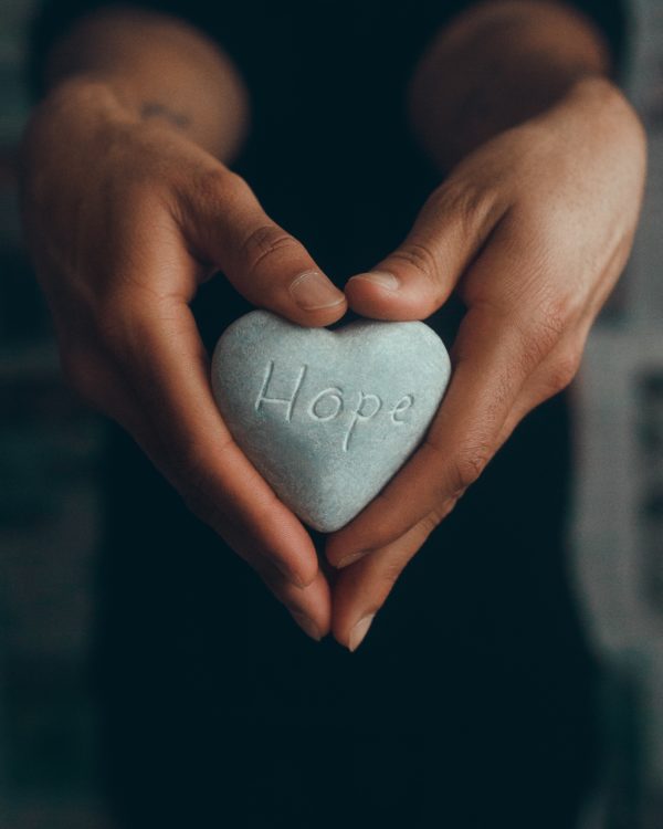 Photo of hands holding heart shape stone that says hope